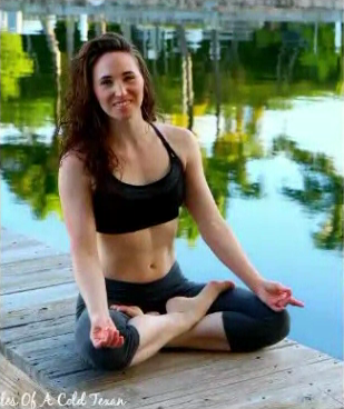 Ashley seated cross-legged on a wooden dock beside the water