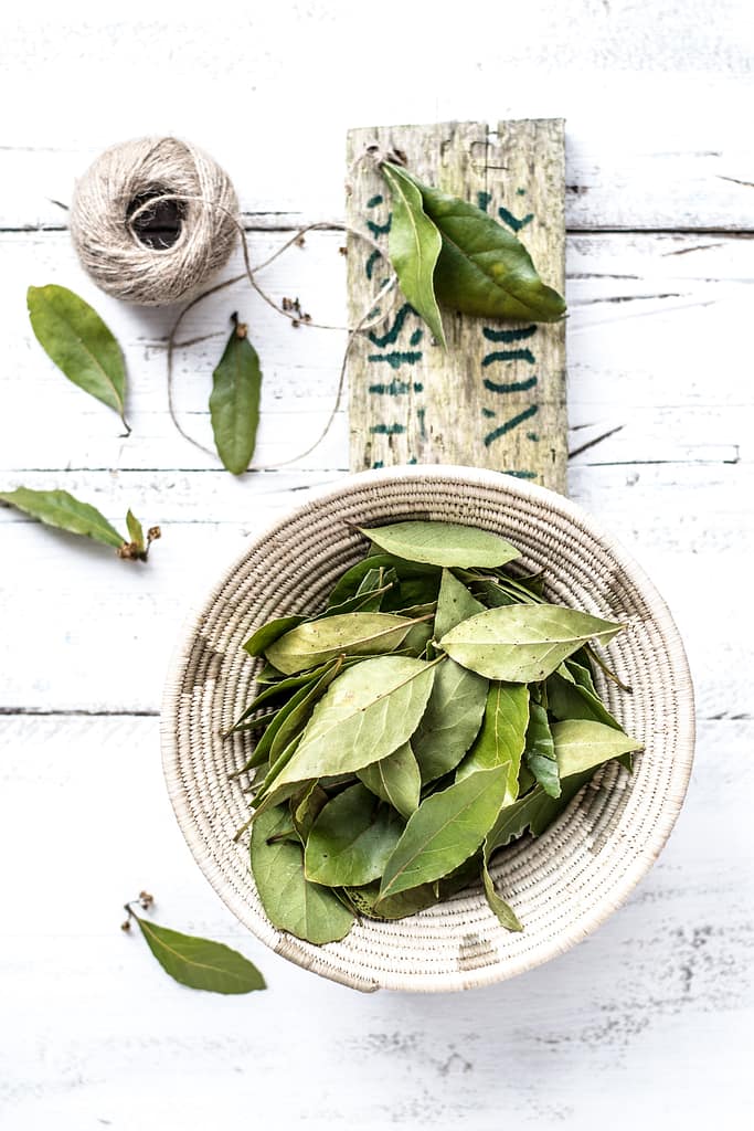 Fresh bay leaves in a woven basket on a white wooden table